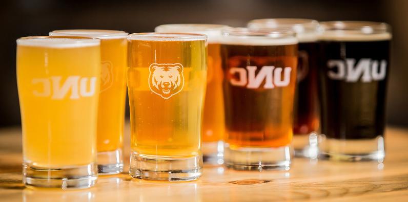 Four beers ranging in colors of brown sitting on a table with a bear logo and UNC on the clear glasses