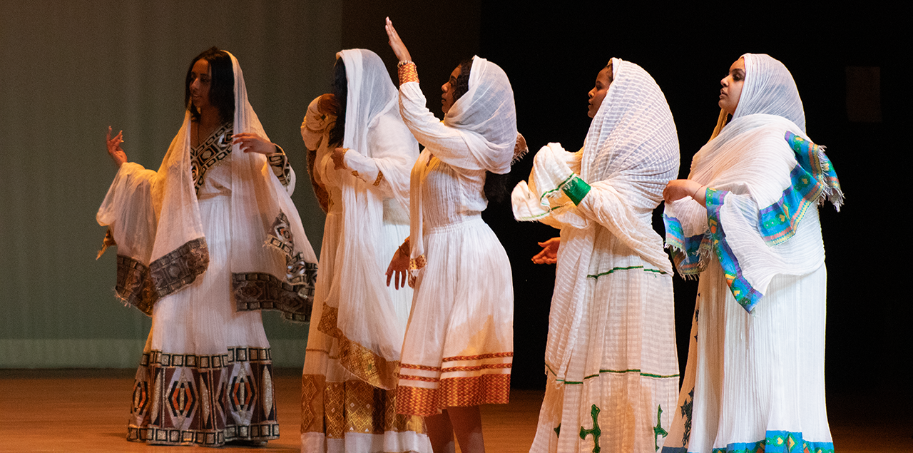 Women wearing white gowns dancing together on a stage