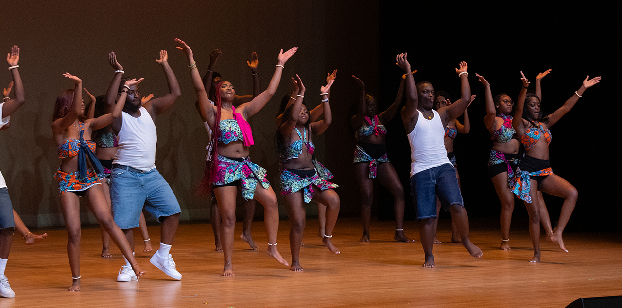 A group of dancers on a stage mid dance with their right arms up