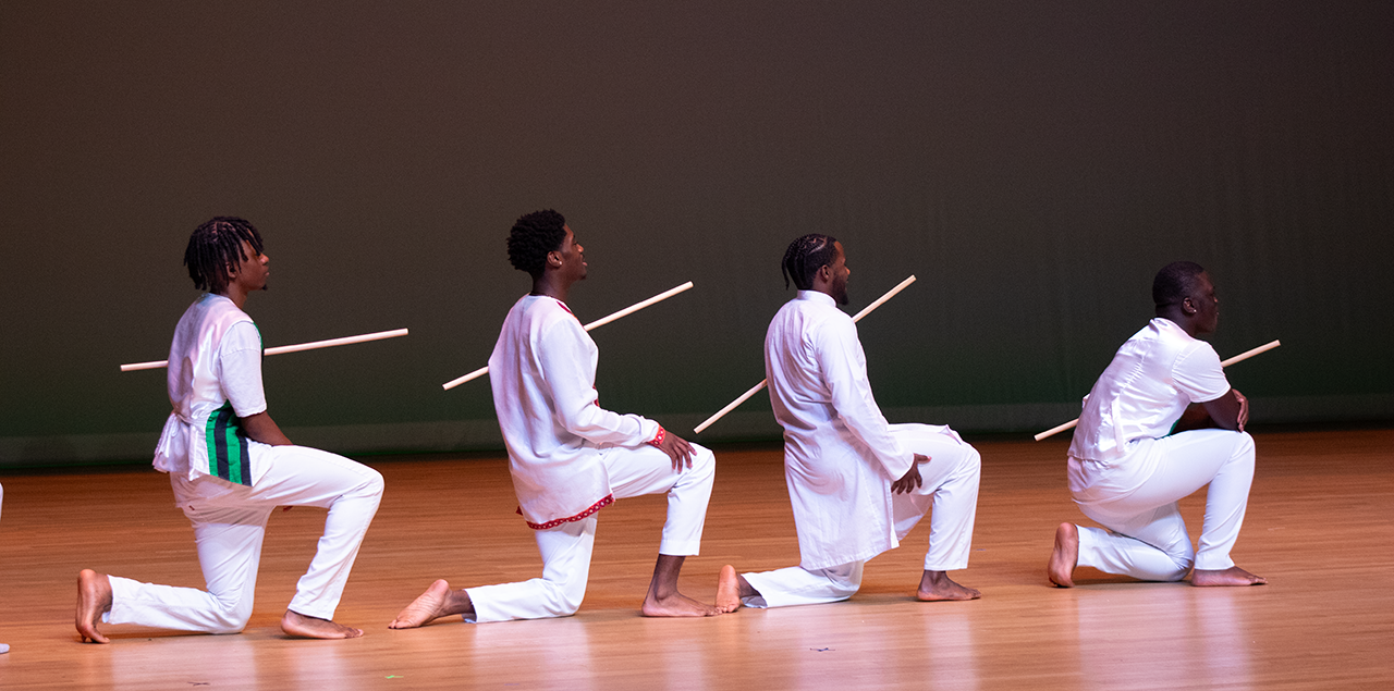 Four men kneeling on their knees in a dance on a stage