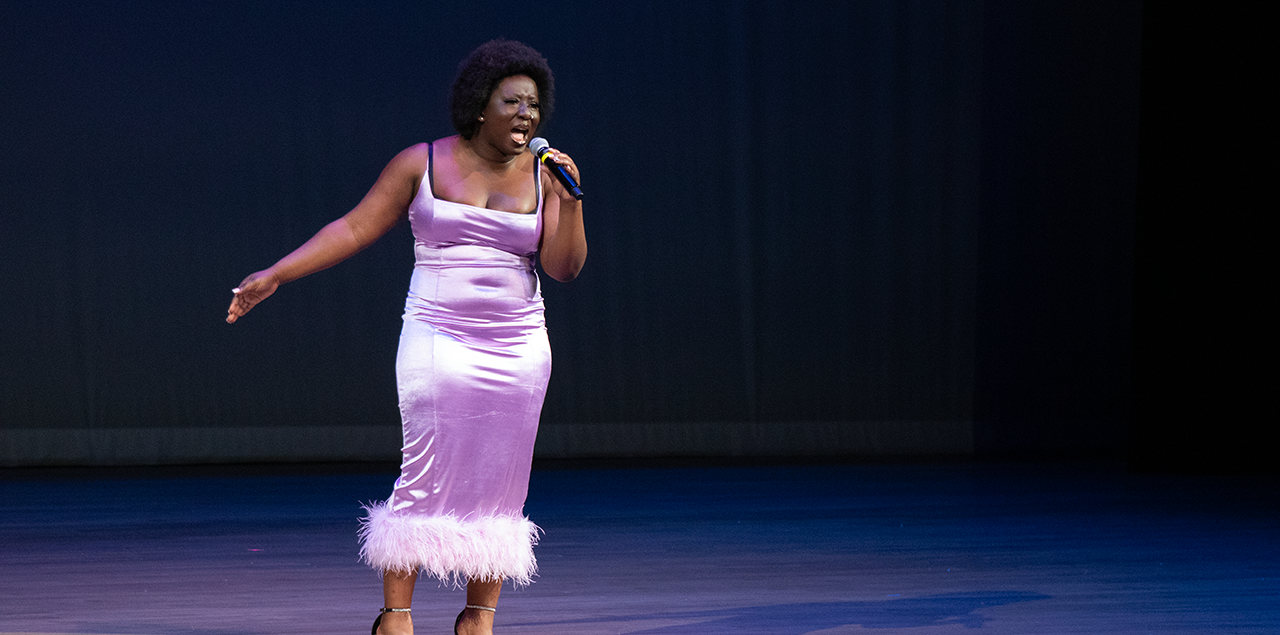 A woman wearing a purple dress singing on stage